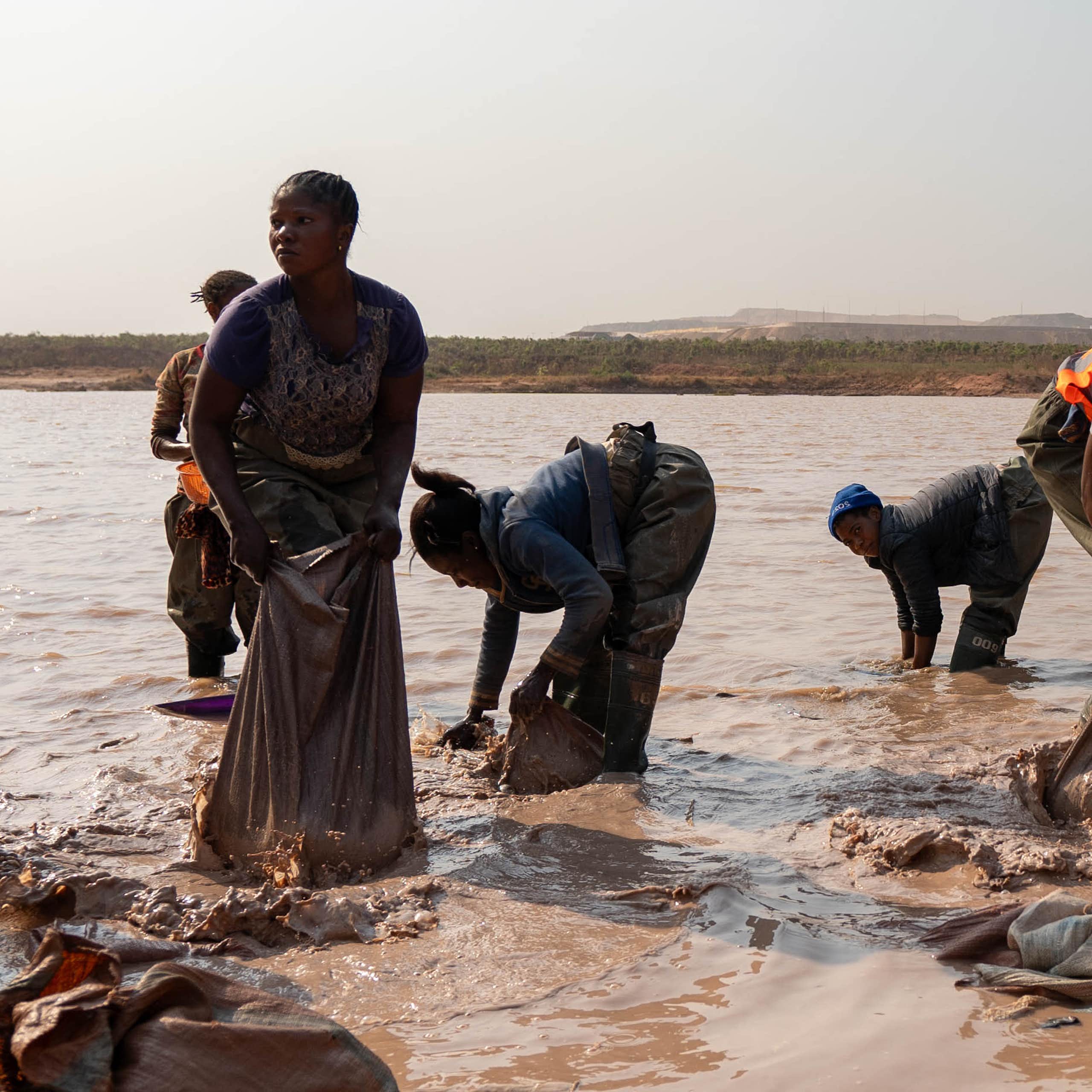 A group of women in a muddy lake, washing something in bags and buckets