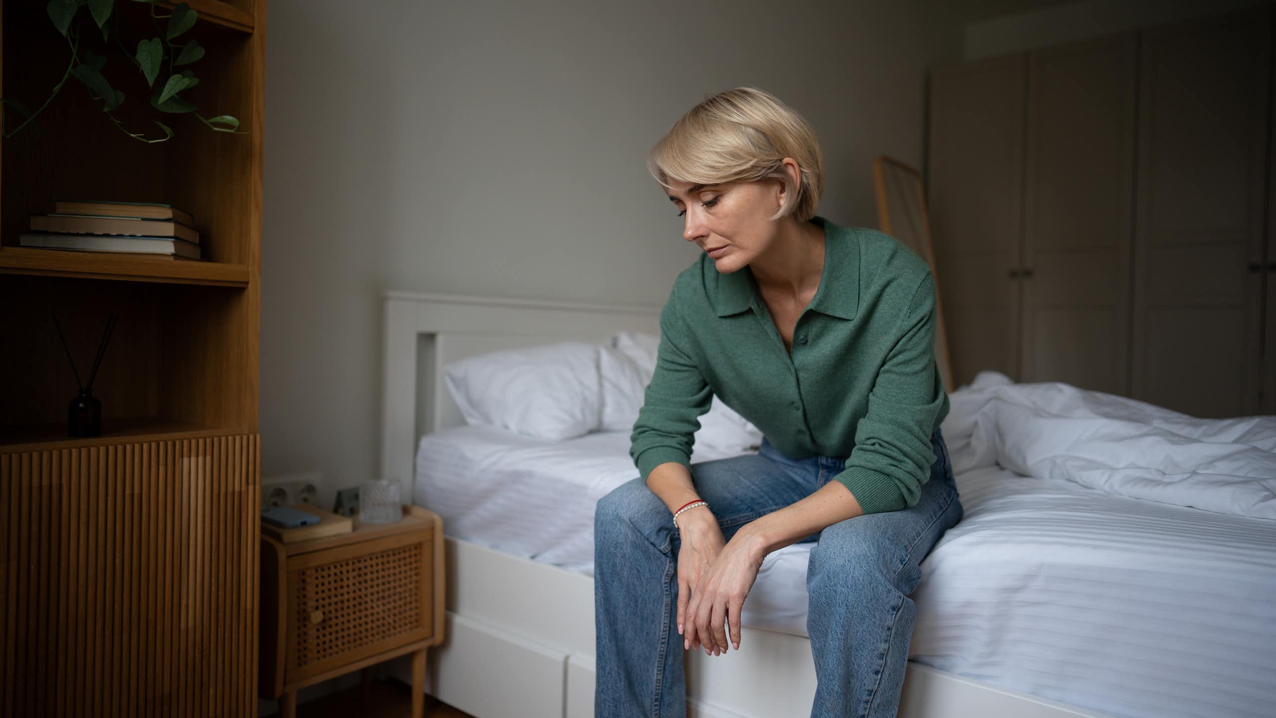 Tired looking woman sitting on the edge of a bed.