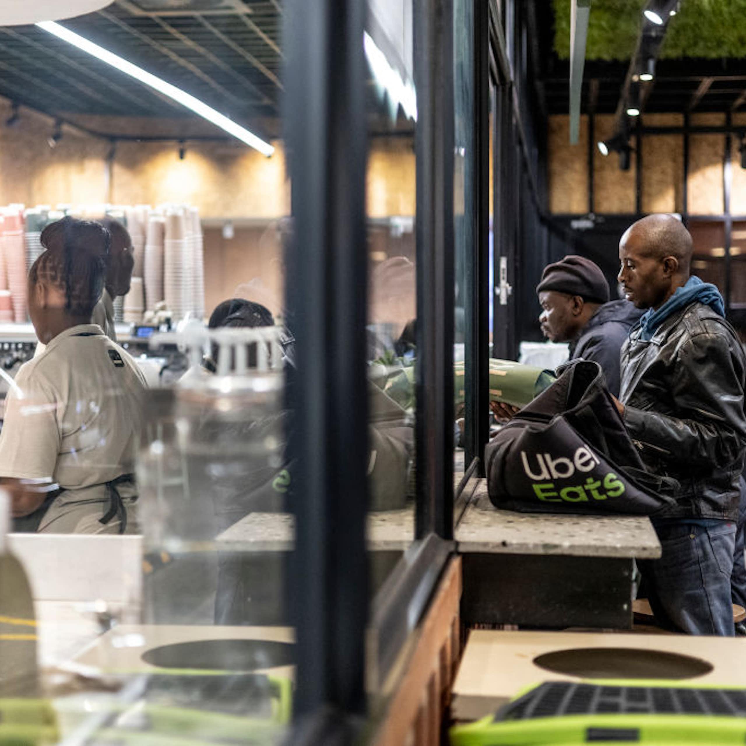 Men with delivery bags stand at the windows of a food outlet