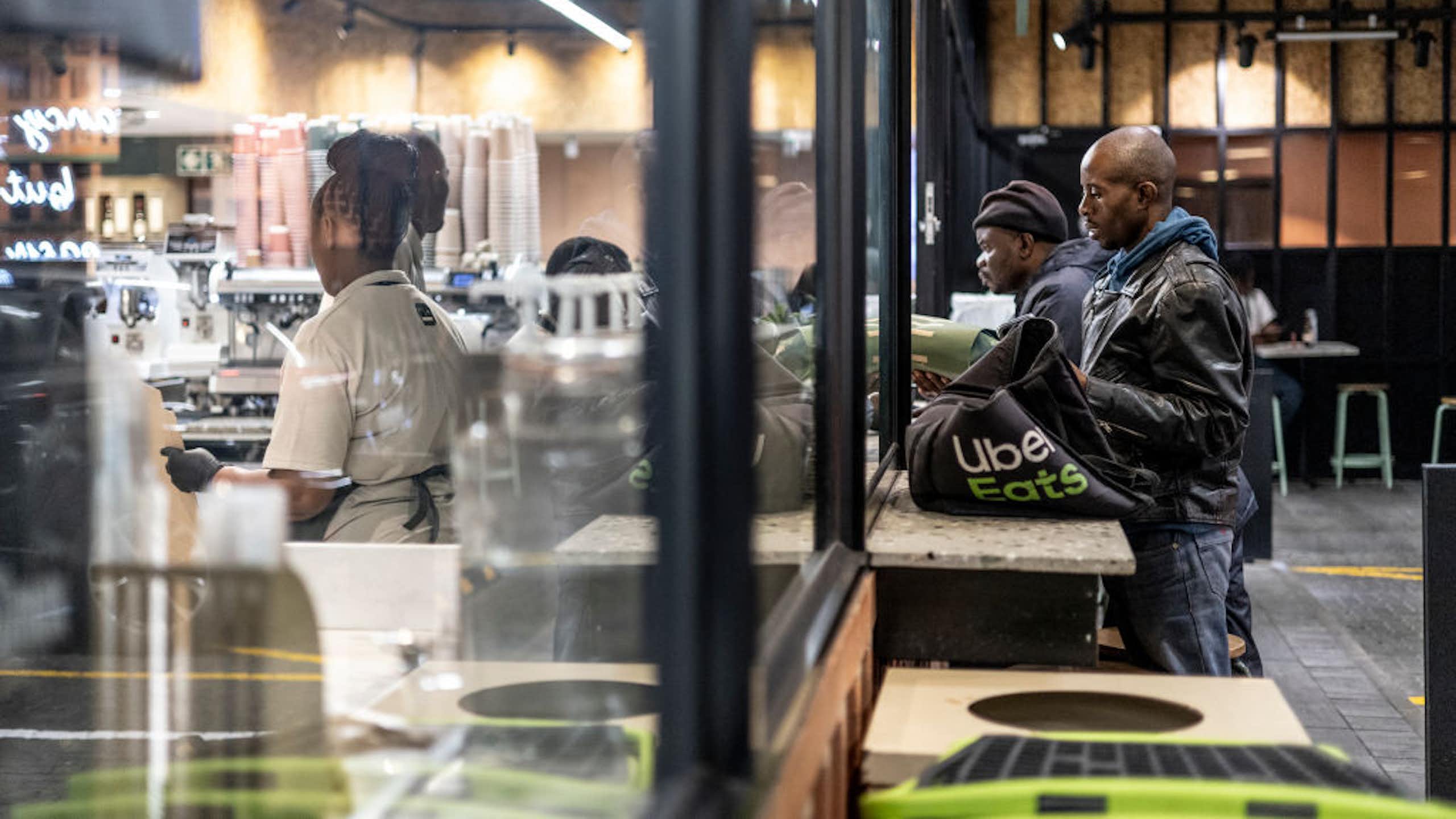 Men with delivery bags stand at the windows of a food outlet