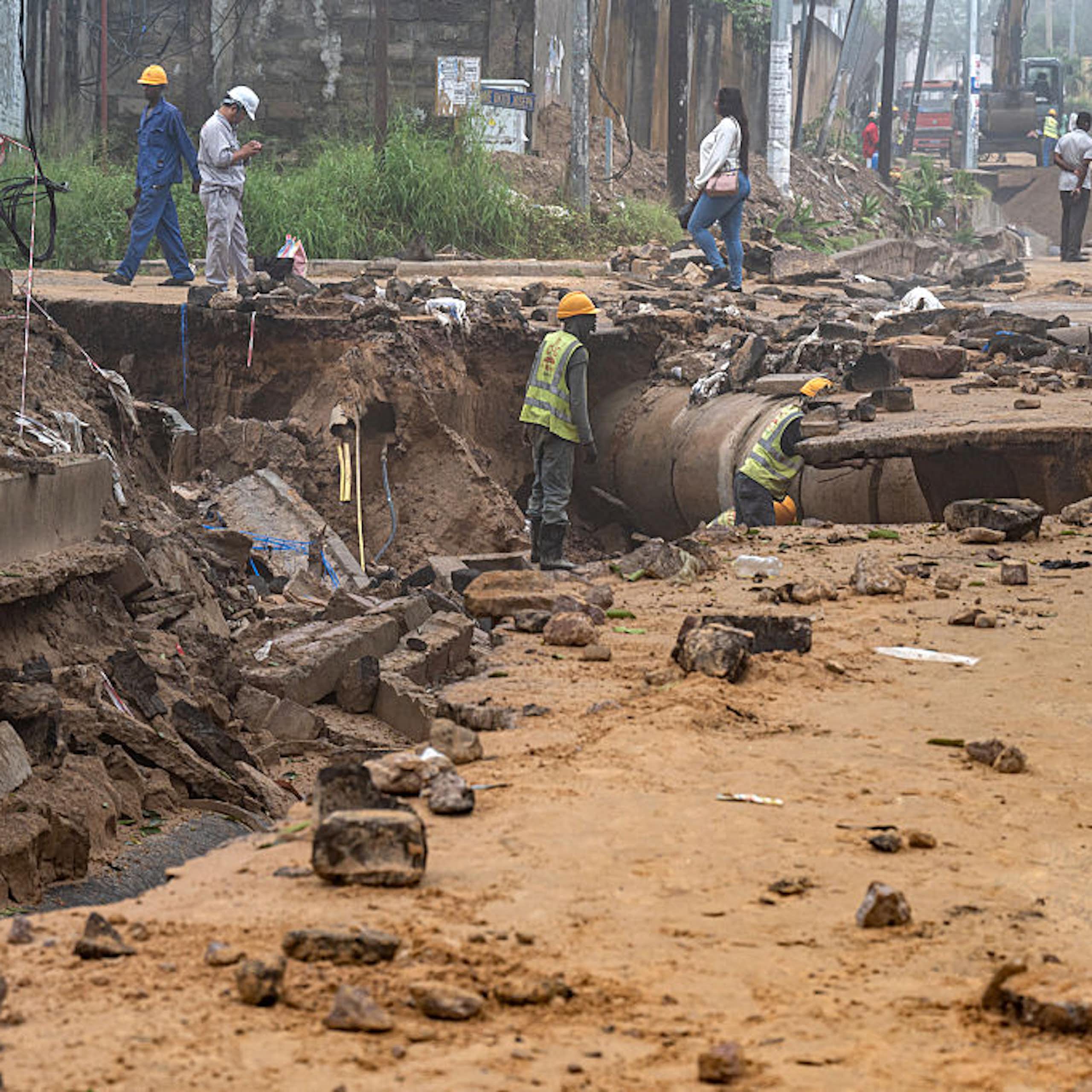 Workers in hard hats looking at a road that has been damaged