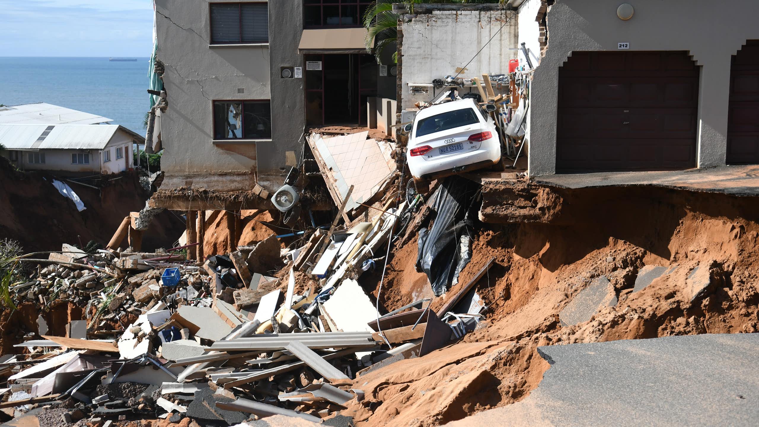 An urban four-storey building where the bottom storey and a parking lot have been washed away by floods