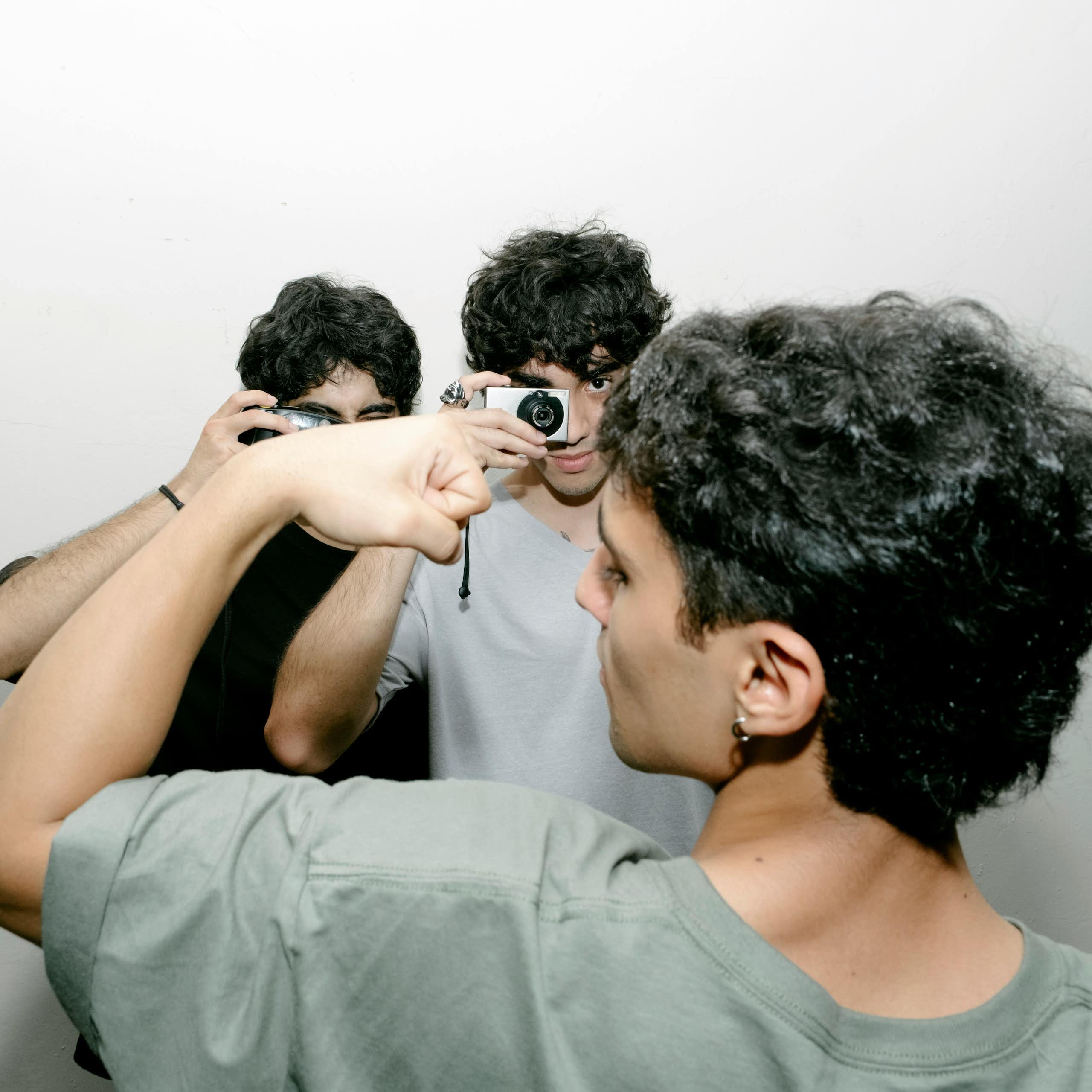 A young man flexing while two others are taking photographs of him.