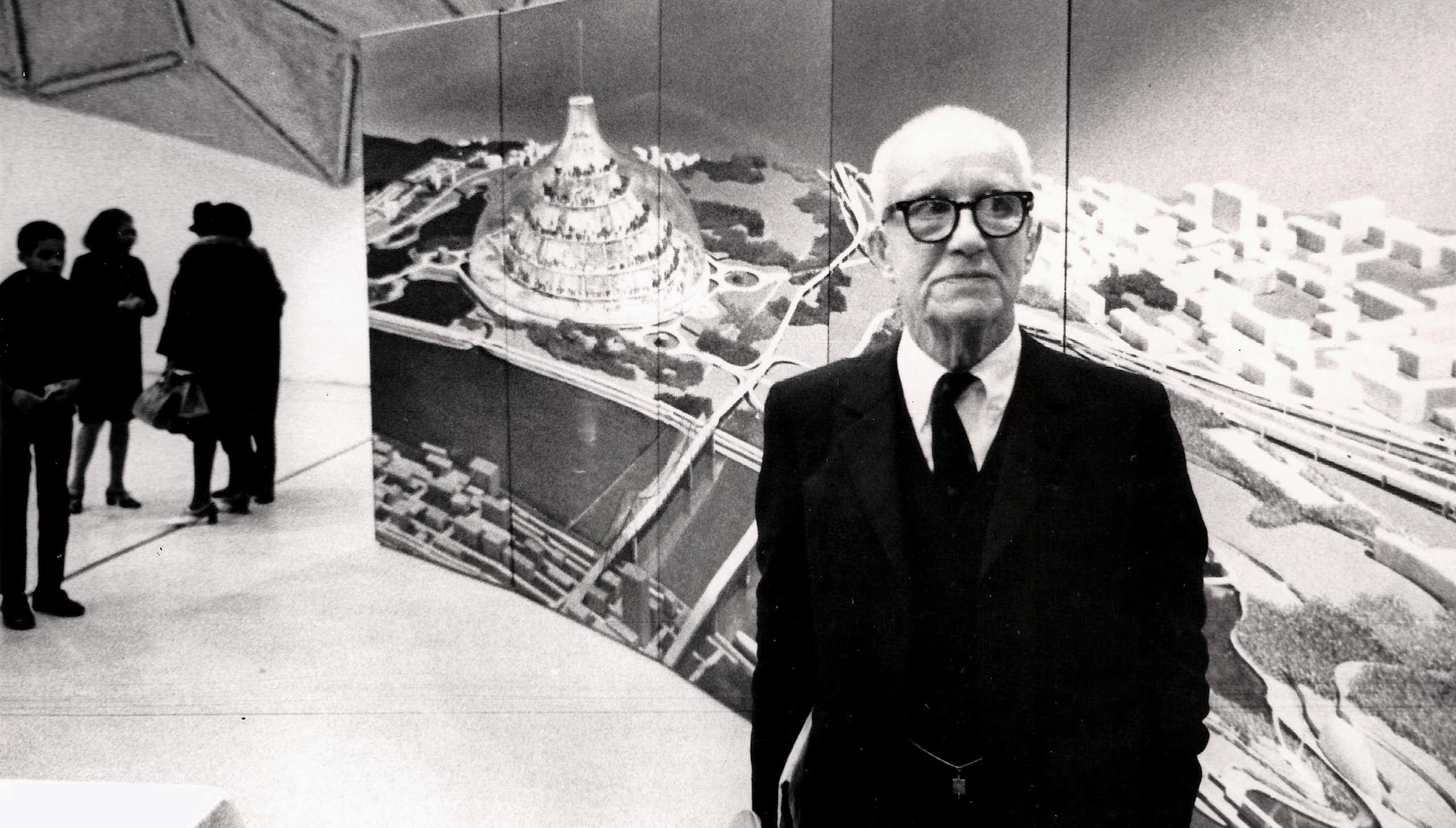 Buckminster Fuller stands in front of a large image of his radical design for a domed city, 1971.
