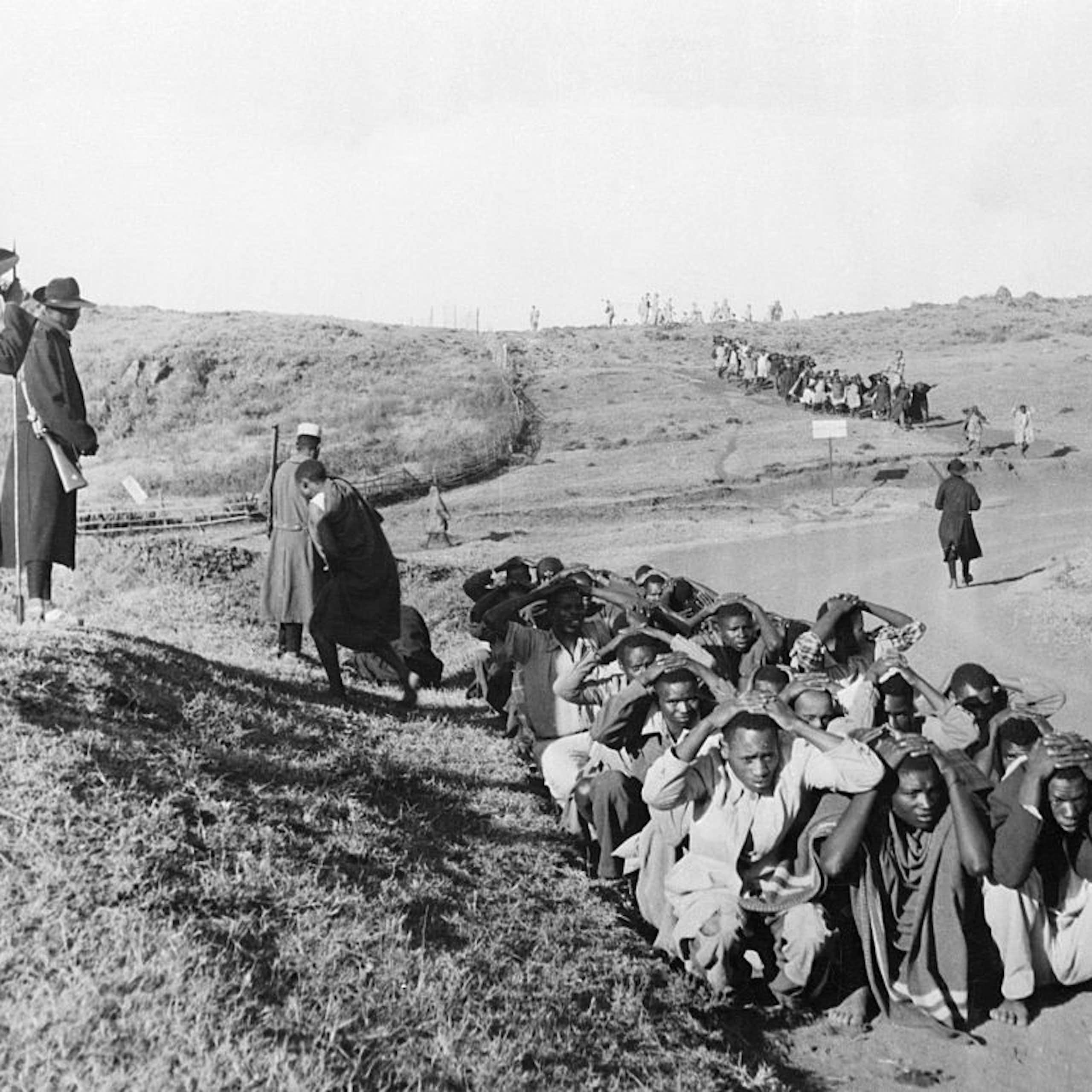 Men huddled on the ground while two others stand towering over them.