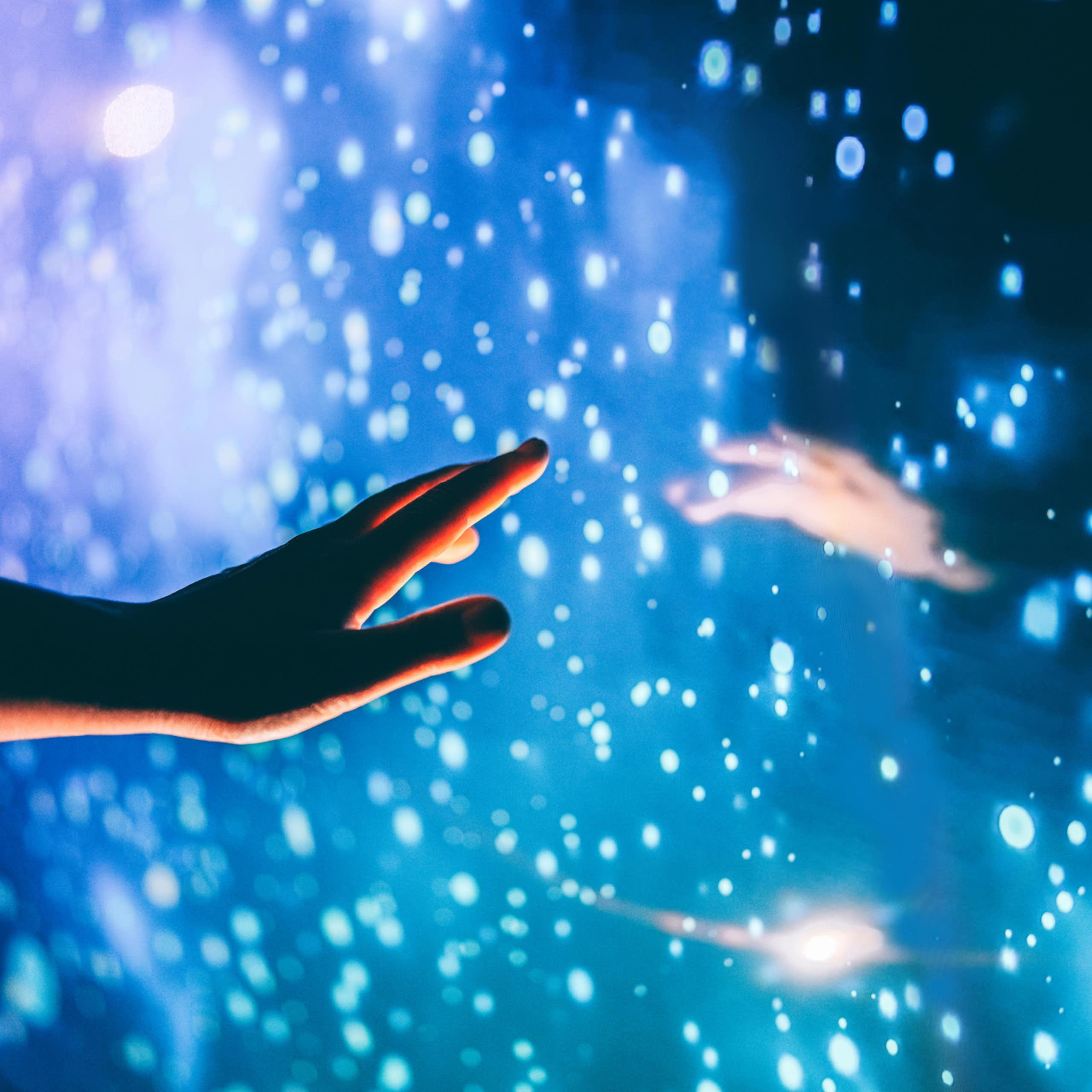 Hand reaching out to a dark, glowing surface with white circles of light, a reflection of another hand reaching back