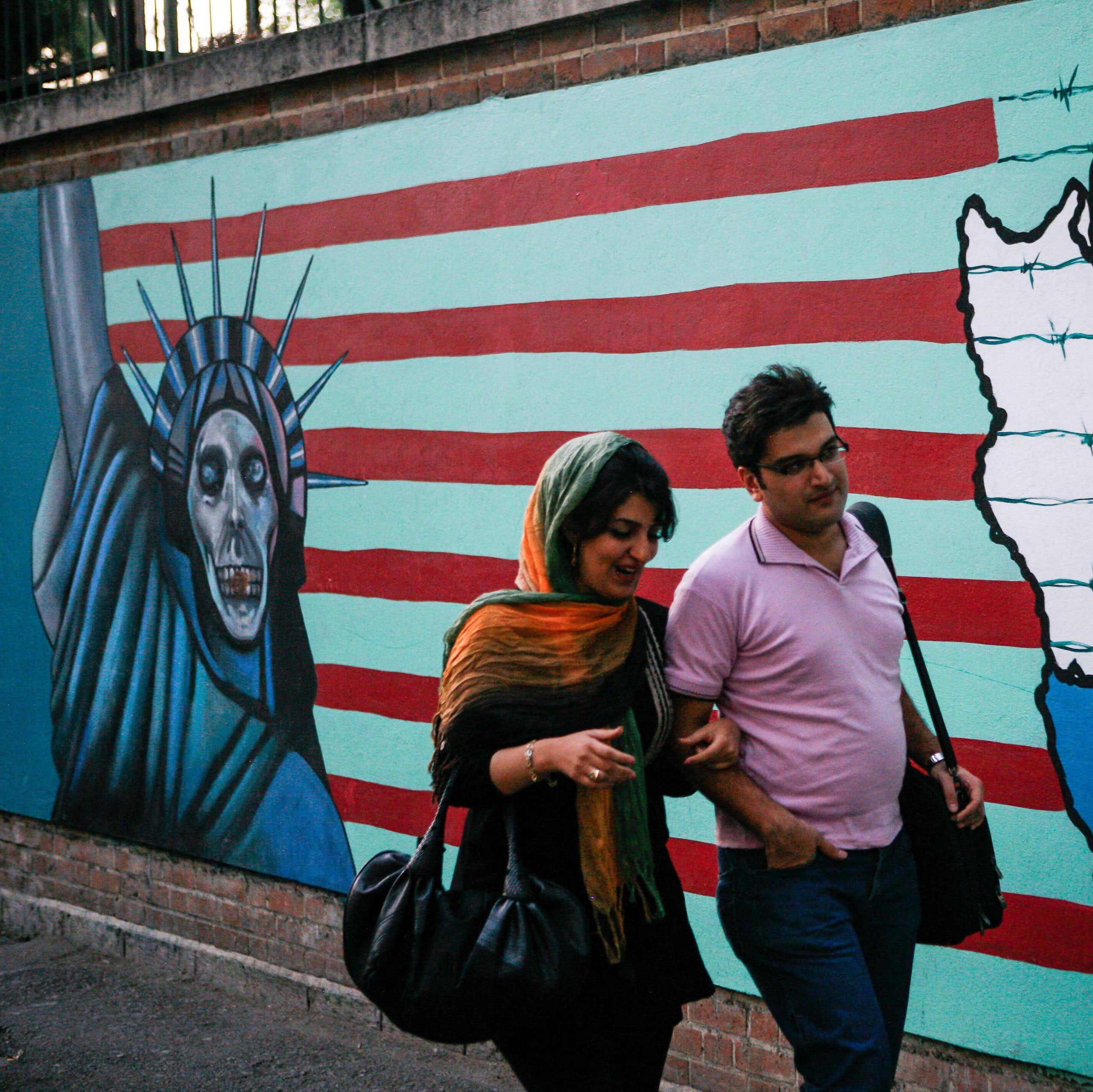 A man and woman walk past an anti-US mural on the walls of the former US embassy in Tehran.