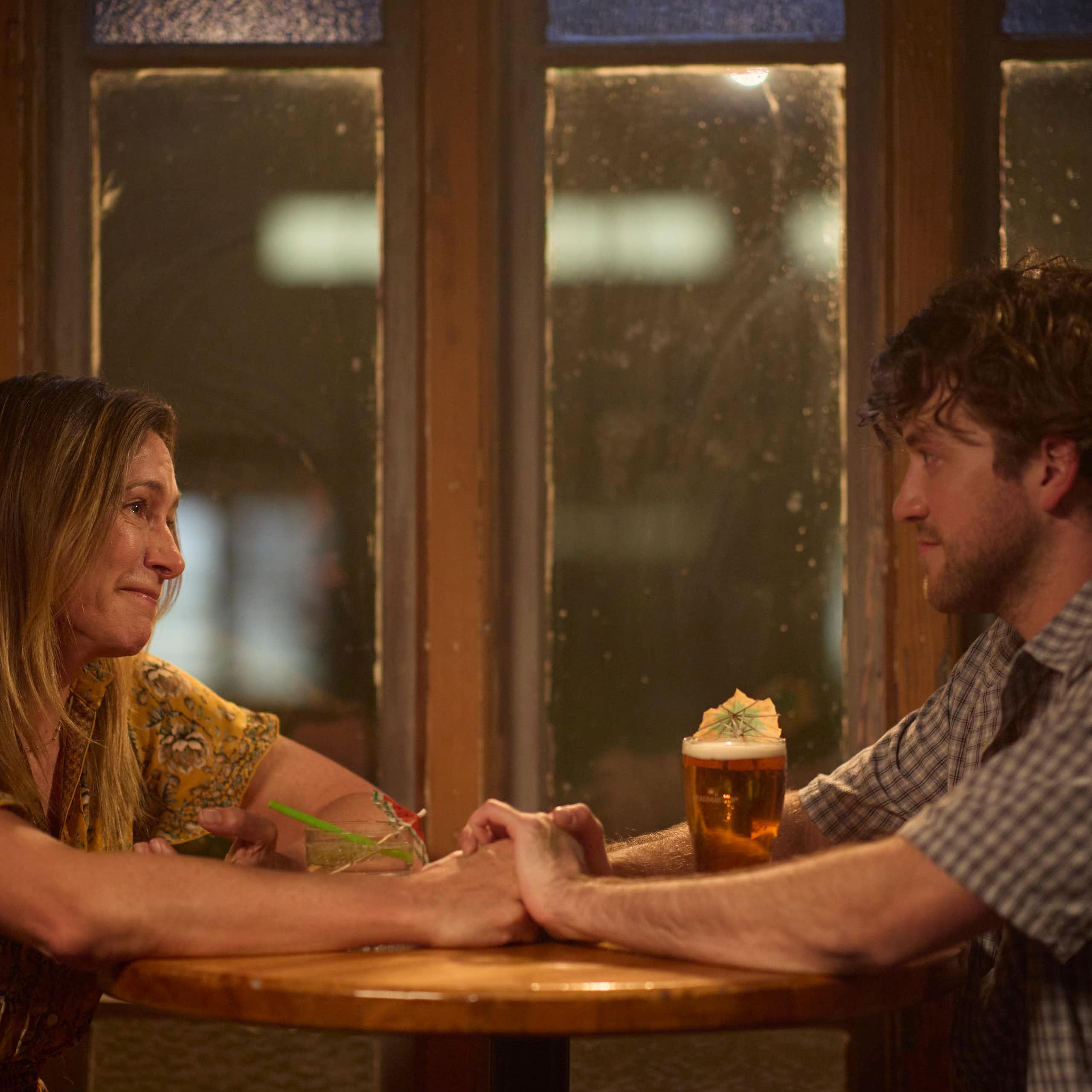 Production image: mother and son hold hands across a table. 