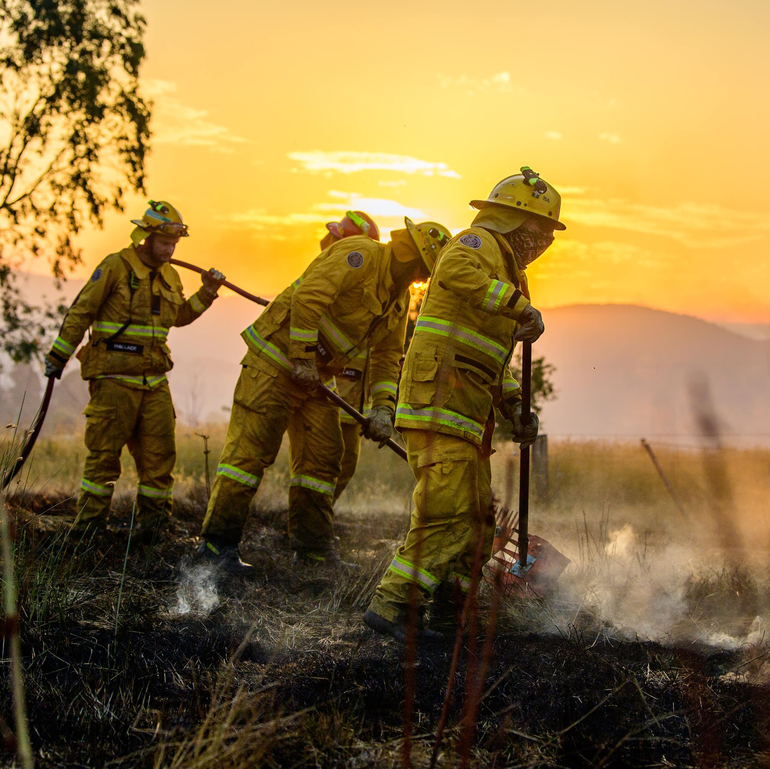 Three firefighters put out a bushfire, with an orange sky in the background.