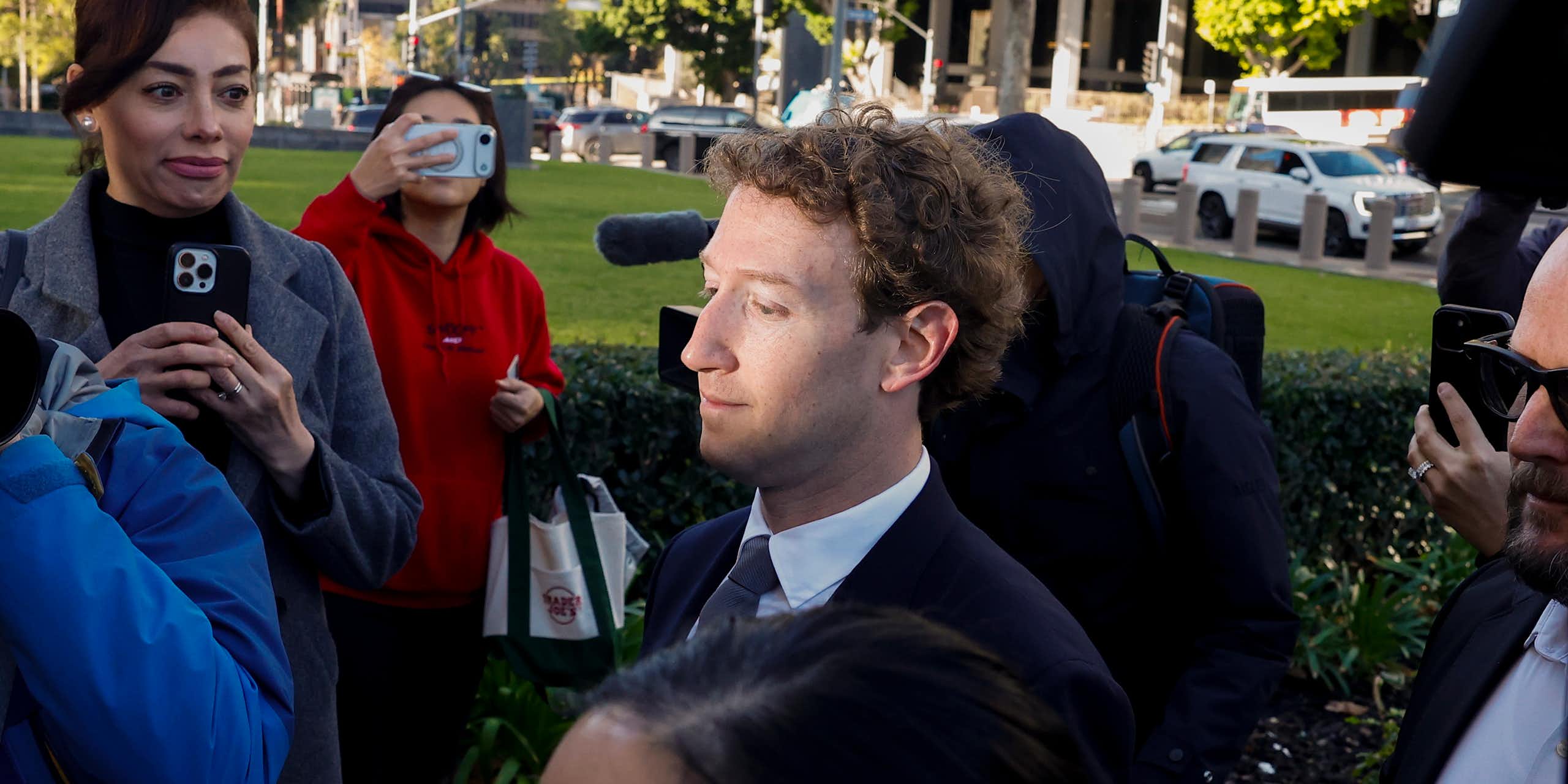 A man walking through a press pack, sunlight on his face.