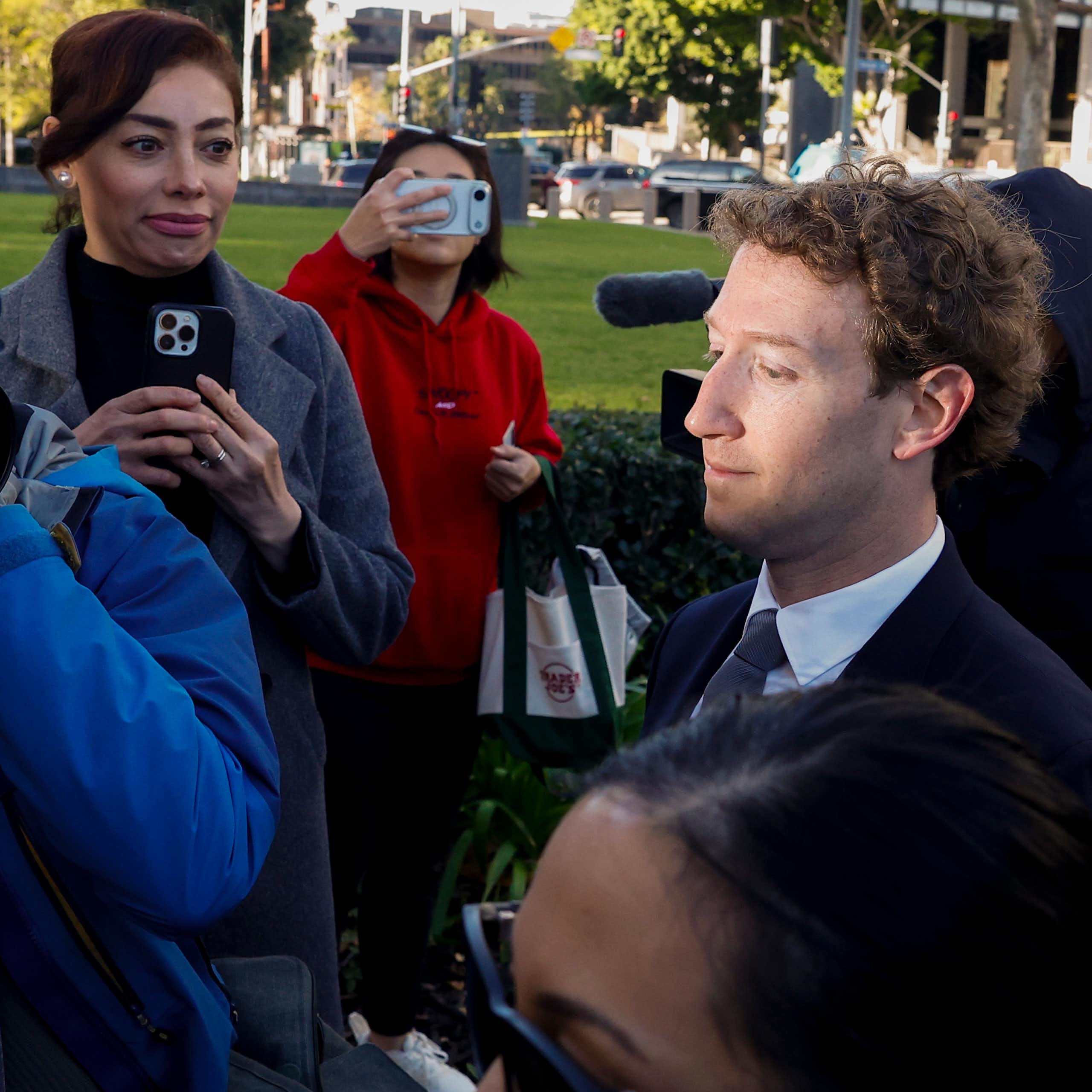 A man walking through a press pack, sunlight on his face.
