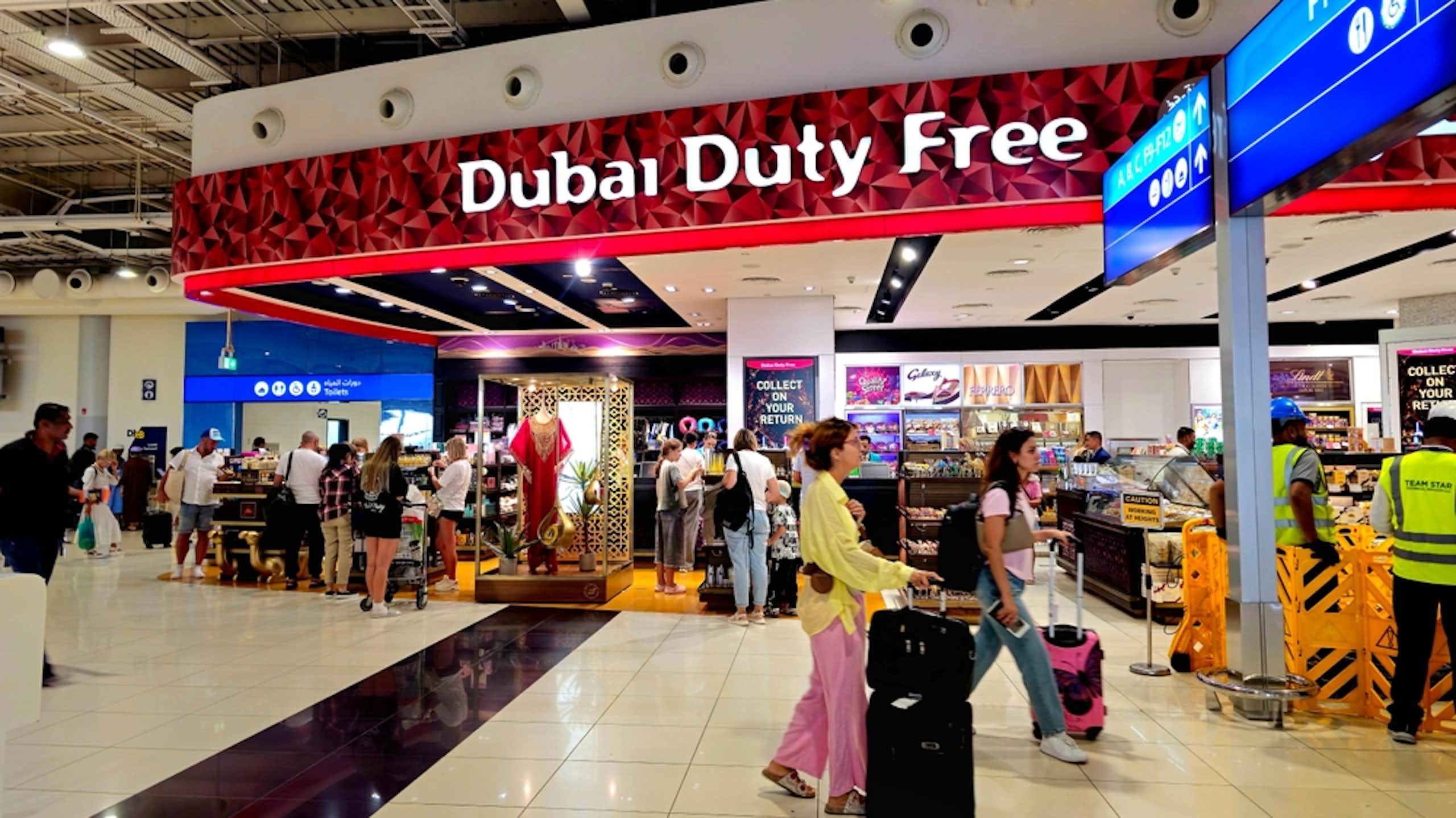 People with suitcases walk in front of a sign that reads "Dubai duty free"