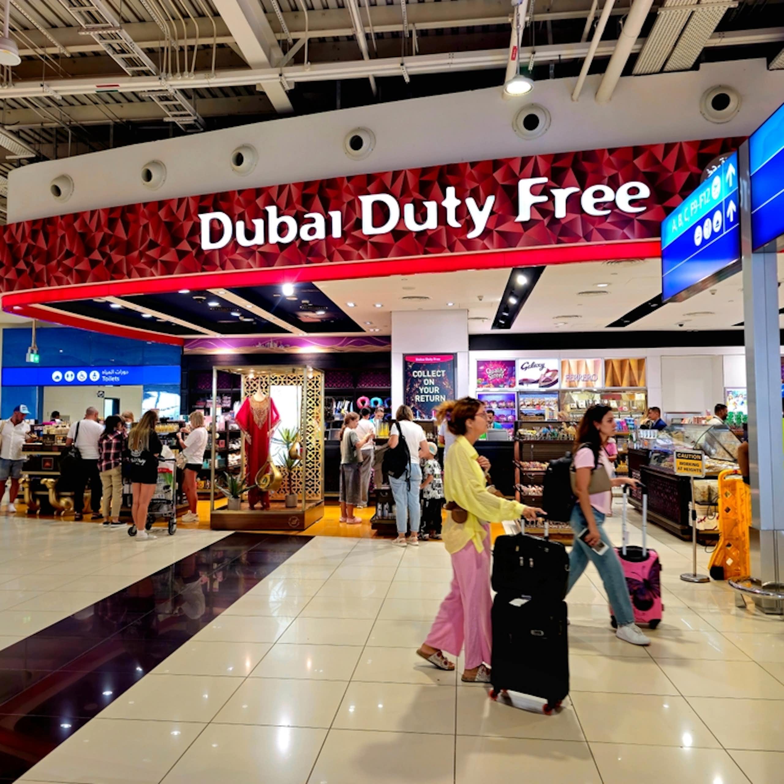 People with suitcases walk in front of a sign that reads "Dubai duty free"