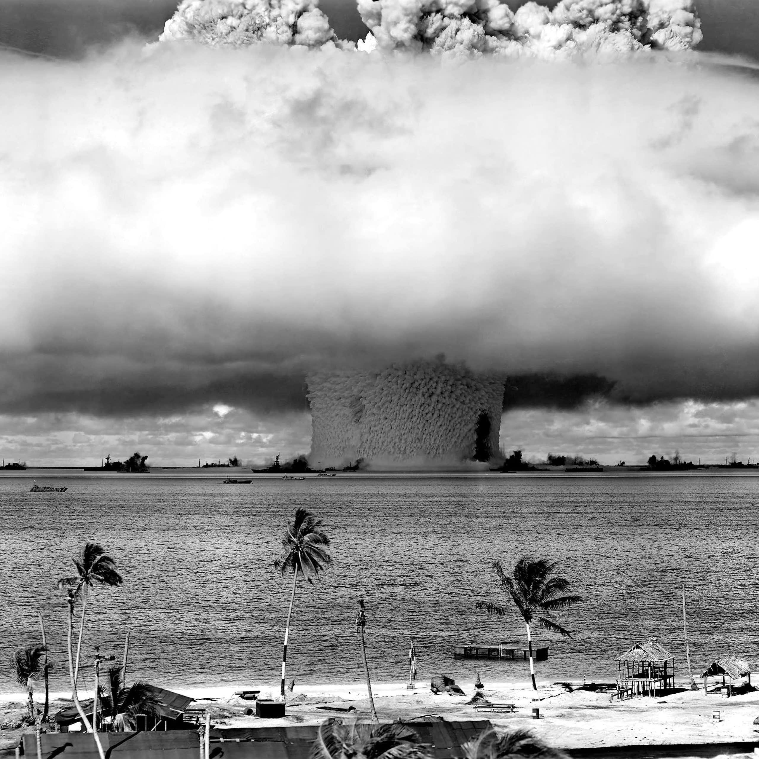A large mushroom cloud spreads above a beach and water.