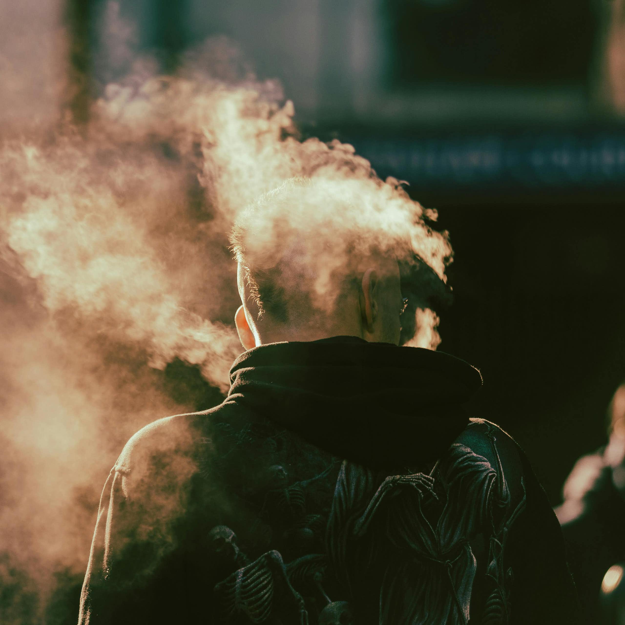 Back of a man vaping with mist around his head.
