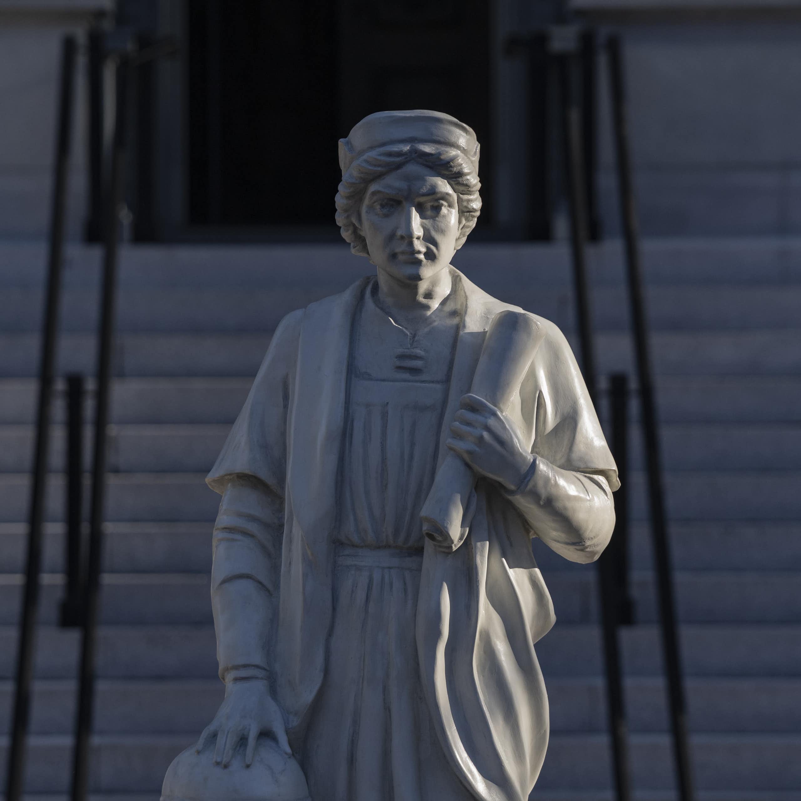 Statue of a man holding a scroll, with stairs in the background