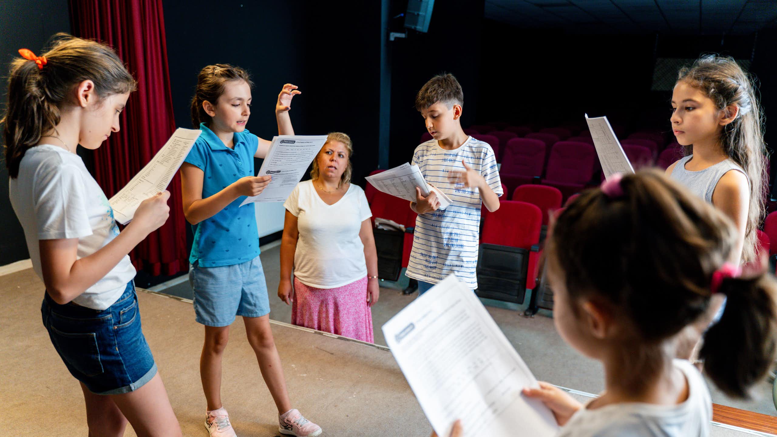 A group of children read scripts on a stage. 
