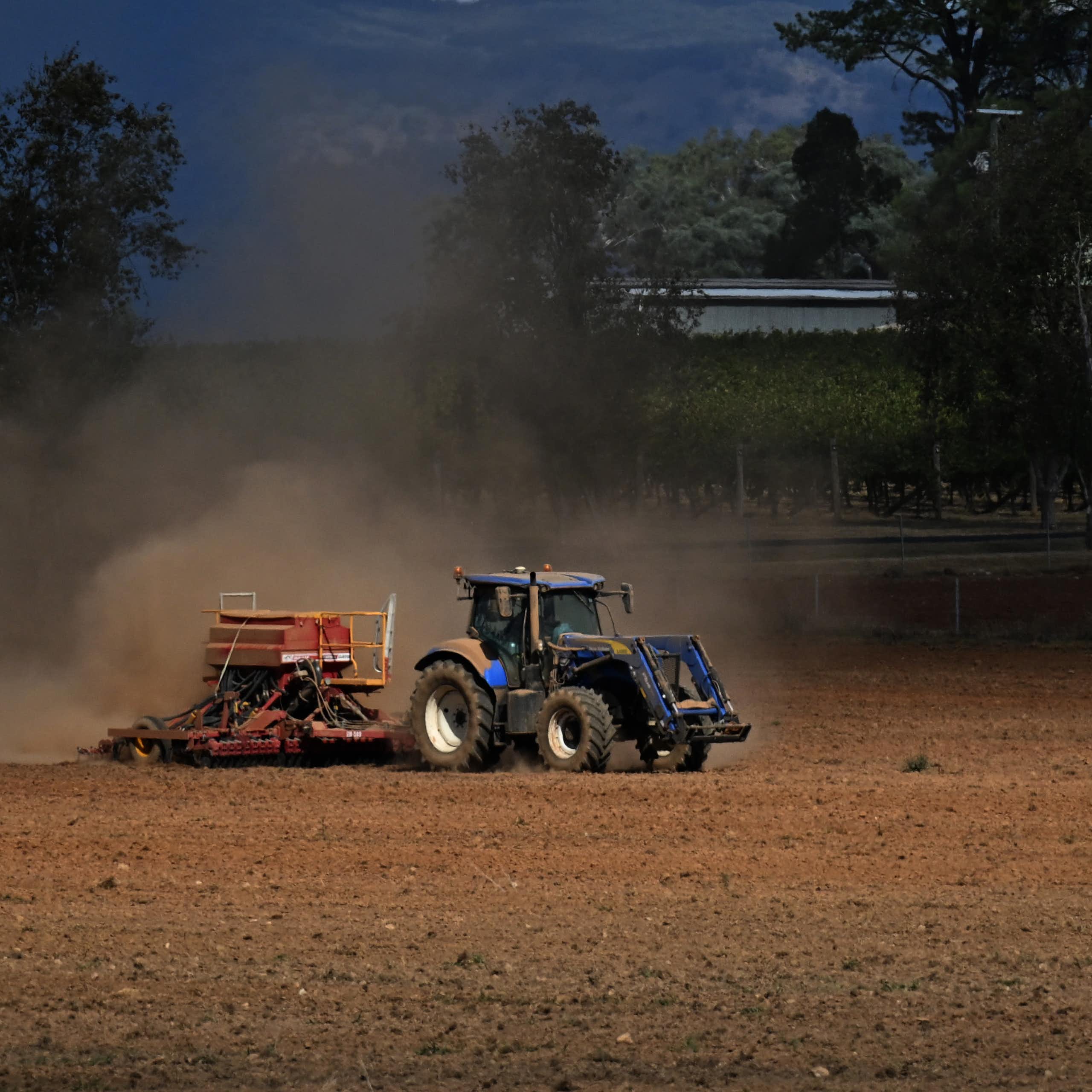 A tractor ploughs a dusty orange field. 