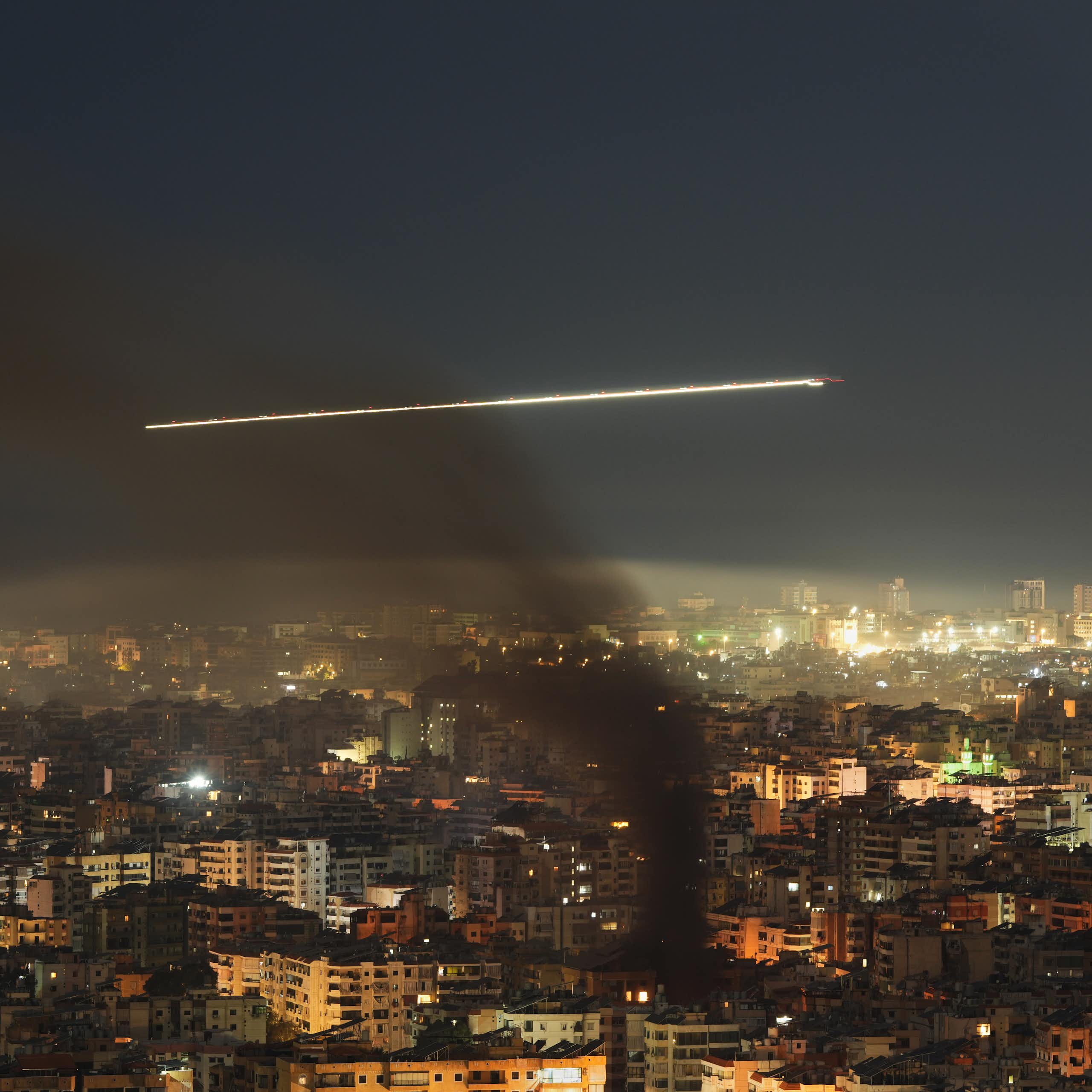 A commercial jetliner flies through black smoke over a city at night.