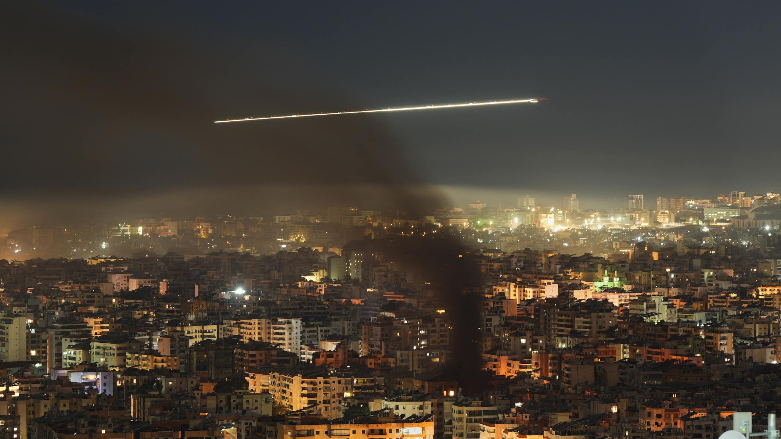 A commercial jetliner flies through black smoke over a city at night.